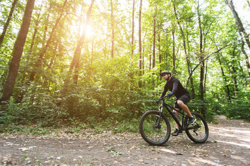 Wall Mural - Male cyclist riding on forest trails in sun flare