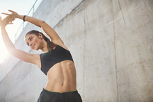 Low-angle Shot Pleased, Motivated Sporty Fitness Woman In Sportsbra And Shorts, Lift Hands Up Stretching, Do Morning Exercise, Warm-up Body Before Marathon, Smiling Stand Concrete Wall On Street