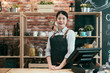 © PR Image Factory - asian korean woman barista standing at billing counter of her cafe posing. Smiling restaurant owner beside the cash machine. elegant bartender looking at camera with charming face in coffeehouse