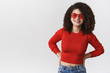 © Cookie Studio - Attractive friendly lively european girlfriend curly dari hairstyle wearing stylish red sunglasses cropped top hold hands waist grinning talking enjoying conversation, standing white background