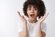 © Cookie Studio - Close up surprised charismatic curly-haired girl react incredible amusing surprise shout wow open mouth impressed raise palms astonished receive positive thrilling news, standing white background
