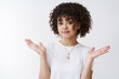 © Cookie Studio - Who cares. Unaware relaxed stylish alluring young curly-haired female clueless shrugging hands spead sideways smirking cannot help have no idea, sorry not know gesture, white background