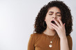 © Cookie Studio - Girl uninterested falling asleep boring talks. Cute 20s curly-haired female yawning closed eyes cover opened mouth palm feel sleepy tired boredom, need coffee get up early morning work