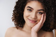 © Cookie Studio - Tenderness, makeup, beauty concept. Headshot attractive tender feminine curly dark hair woman smiling cheerful happiness touch soft clean pure skin cheek tilt head joyful apply skincare cosmetics
