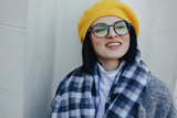 Fototapeta  - Attractive smiling young girl in glasses in coat and yellow Beret on a simple light background