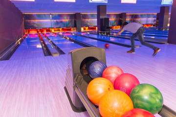 Bowling balls close up and a man throws the ball in a bowling club