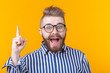 Amazed stupefied bearded handsome man opens mouth wide, raises fore finger as gets idea on yellow background.
