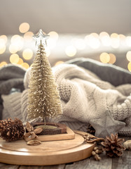 Little Christmas tree over Christmas lights bokeh in home on wooden table with sweater on a background and decorations. Holiday decoration