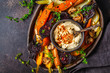 Baked vegetables with hummus in a dark dish, top view.
