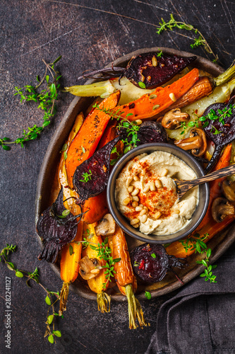 Fotografía Baked vegetables with hummus in a dark dish, top view.