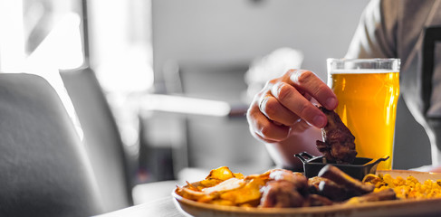 Wall Mural - man hand with glass of cold beer and plate with snacks on wooden table background on bar or pub