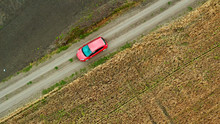 Top View Of A Field With Wheat And A Red Car Moving On The Rural Road. Aerial View From Drone