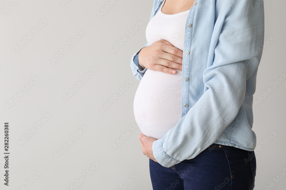 Young pregnant woman on light background