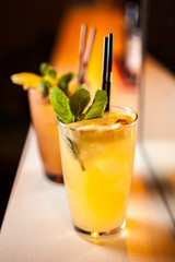 Two orange cocktails with orange and mint on the bar, blurred background.