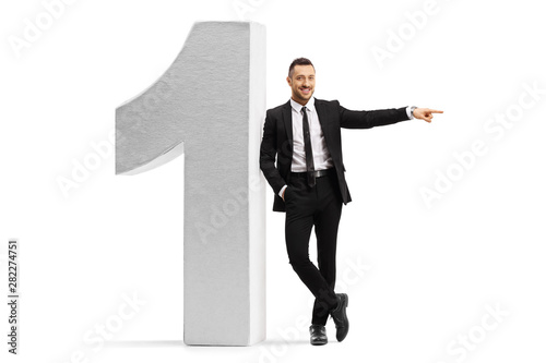 Fotografía Young businessman leaning on a large number one and pointing to the side