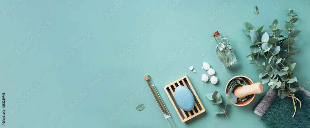 Soap, eucalyptus, towels, massage brush, salt, aroma oil and other spa objects on green background. Top view. Skin care, body treatment concept. Banner. - obrazy, fototapety, plakaty 