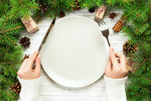 Top View Girl Holds Fork And Knife In Hand And Is Ready To Eat. Empty Plate Round Ceramic On Wooden Christmas Background. Holiday Dinner Dish Concept With New Year Decor