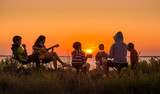 Fototapeta  - people sitting on the beach with campfire at sunset