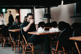 Fototapeta  - Stylish young brunette man sits in a cafe on the terrace and drinks coffee. Italian street