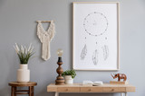 Fototapeta Boho - Design home interior of living room with stylish chair and wooden desk, plants, flowers, table lamp, mock up poster frame, macrame and elegant accessories. Stylish home decor. Template. Gray walls. 