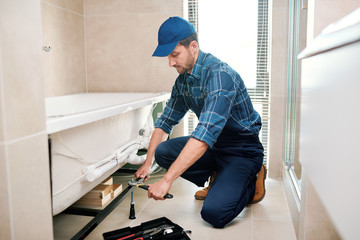 Young plumber or technician preparing detail for bathtub installation