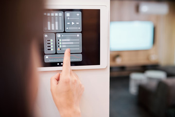 Hand of young woman touching one of digital buttons on smart remote control