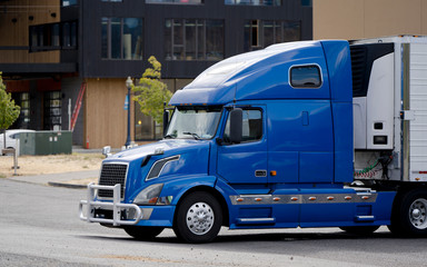 Bright blue bonnet big rig semi truck unloaded commercial cargo from refrigerator semi trailer on the side of delivery in urban city