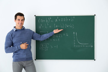 Young teacher explaining math formulas written on chalkboard in classroom