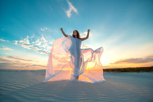 A Girl In A Fly White Dress Dances And Poses In The Sand Desert At Sunset