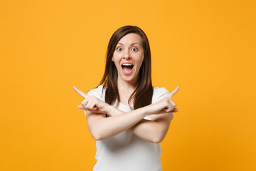 Wall Mural - Surprised young woman in white casual clothes keeping mouth open pointing index fingers aside, holding hands crossed isolated on yellow orange background. People lifestyle concept. Mock up copy space.