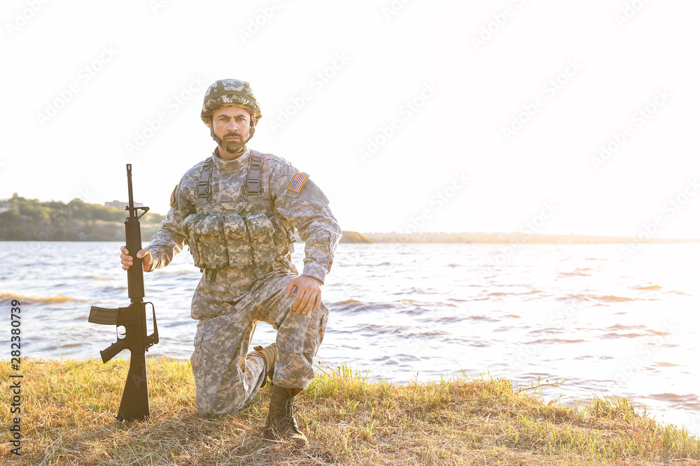 Soldier in camouflage with assault rifle near river