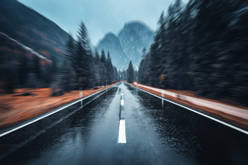 Wall Mural - Road in the autumn forest in rain with motion blur effect. Perfect asphalt mountain road in overcast rainy day with blurred background. Roadway in motion. Transportation. Empty highway. Fast driving