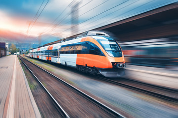 Wall Mural - high speed orange train in motion on the railway station at sunset. modern intercity passenger train