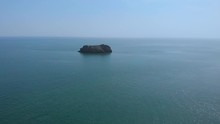 An Aerial Backward Footage Of Two Islands Rock, Two Kayakers And A Rocky Coastline With Turquoise Water Under A Majestic Blue Sky