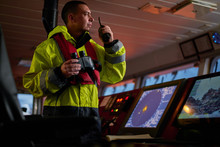 Navigator. Pilot, Captain As Pat Of Ship Crew Performing Daily Duties With VHF Radio, Binoculars On Board Of Modern Ship With High Quality Navigation Equipment On The Bridge On Sunrise.