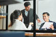 © DragonImages - Young business people pointing at document in businessman's hands and discussing at meeting behind the glass wall at office