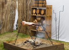 Lamb Is Cooked On A Skewer Over A Fire Of Birch Wood. In The Background, A Wicker Fence, On The Rack Are Oak Barrels And Pumpkins