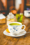 Fototapeta Morze - green tea matcha soy latte in a china cup with brown sugar and a glass of water on the side
