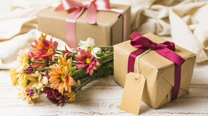 Brown wrapped gift with empty tag and beautiful flower bouquet