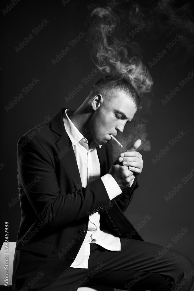 Contrast portrait of a Smoking man businessman in an expensive business  suit on a dark background. Successful emotional Manager businessman posing  gestures hands and Smoking cigarette on a black Stock Photo |