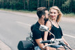 © LIGHTFIELD STUDIOS - happy young couple of bikers looking at each other on black motorcycle on road