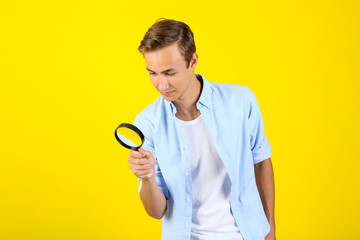 Canvas Print - Young man with magnifying glass on yellow background