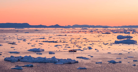 Wall Mural - Ice and Icebergs from glacier - amazing arctic nature landscape aerial image of icefjord filled with icebergs from melting glacier Sermeq Kujalleq, Ilulissat, Greenland. Fishing boat and Midnight sun.