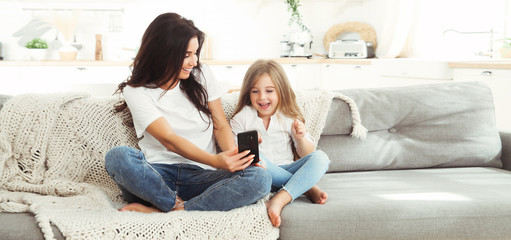 Smiling mother and little daughter playing games with smartphone. Panoramic banner copy space