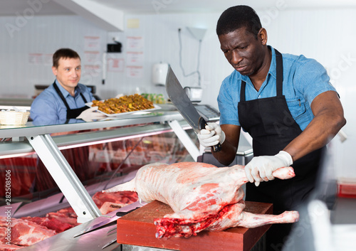 Cuadros en Lienzo Skillful African American butcher processing carcase of young lamb for sale at b