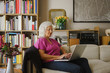 © fStop - Senior woman using laptop on living room sofa