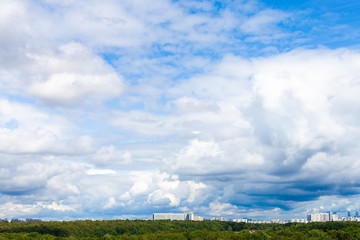 Wall Mural - low large white clouds in blue sky over city park