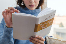 Close-up Of A Girl In A Blue Sweater Reading A Book On Psychology Near The Window