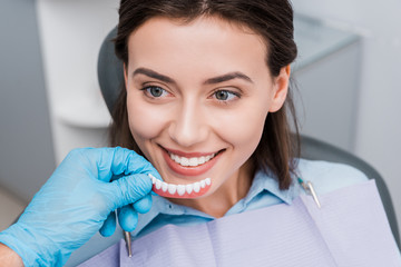 cropped view of dentist holding prosthesis near happy girl in dental clinic