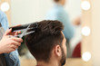 © New Africa - Barber making stylish haircut with professional scissors in beauty salon, closeup